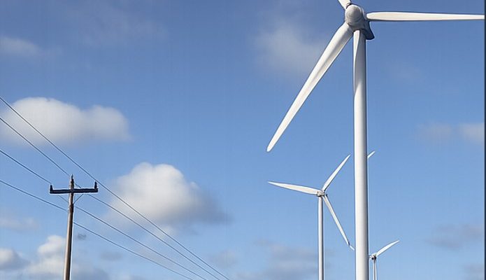 Three white wind turbines with powerlines and blue sky and white clouds in the background.