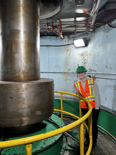 Aleah is dressed in PPE standing in front of a piece of large equipment.