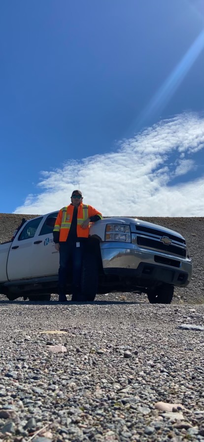 Francis is wearing an orange hi-vis jacket and leaning up against a Hydro fleet vehicle