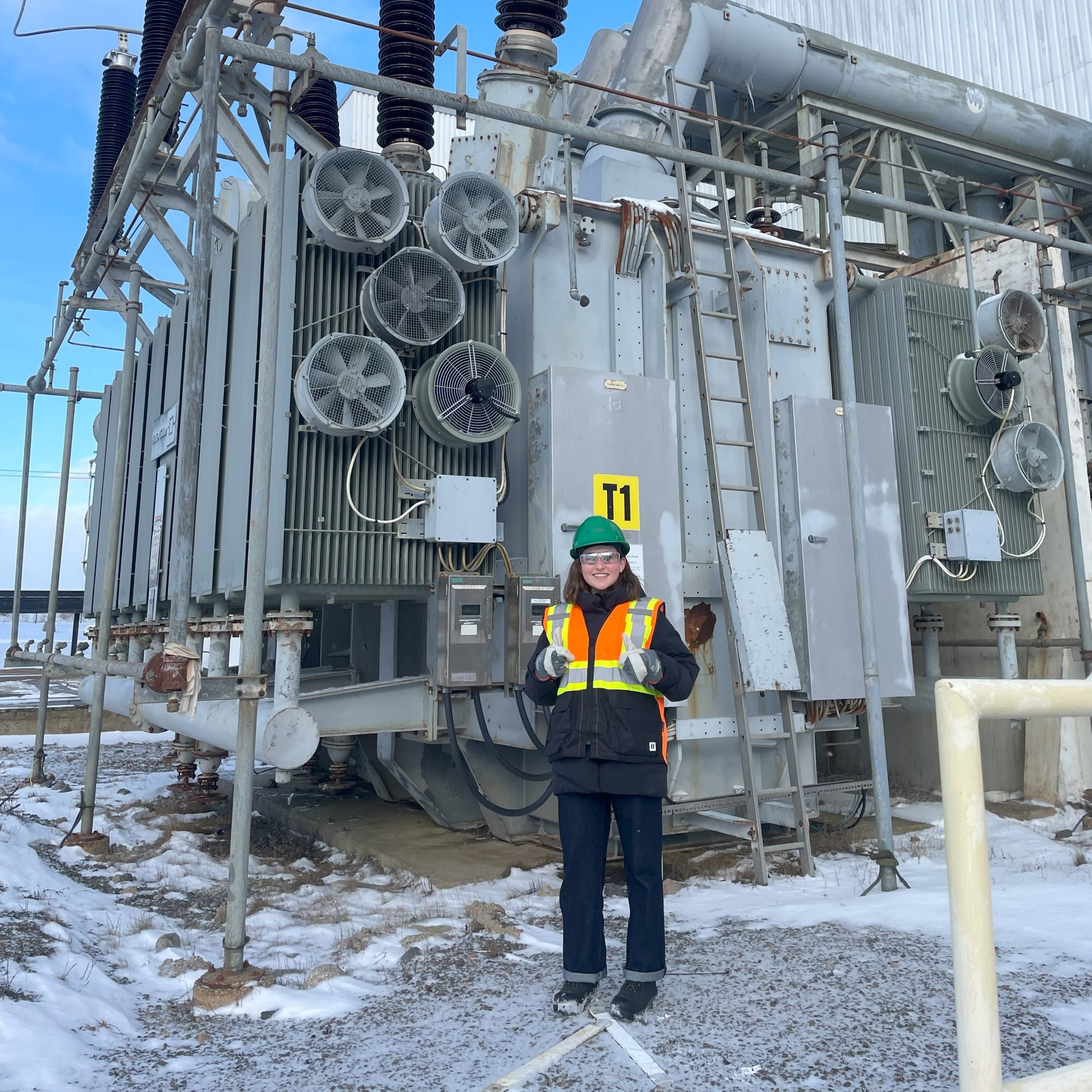 Hannah wears full PPE as she stand in front of a transformer