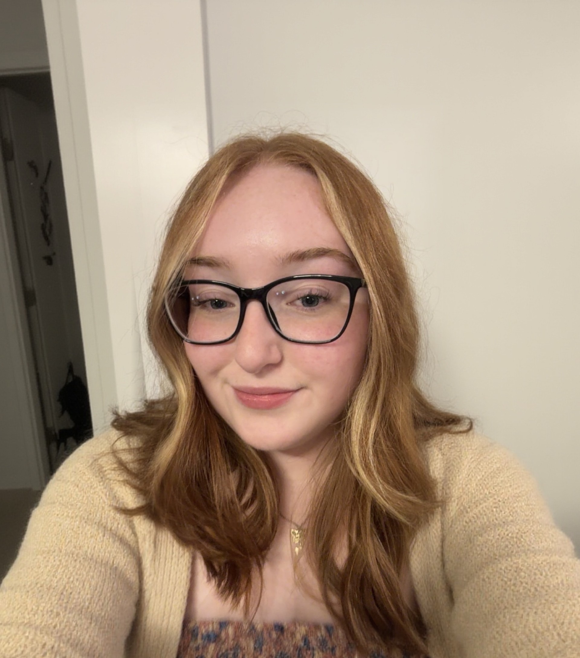 Shawna wears glasses and a beige sweater as she smiles at the camera