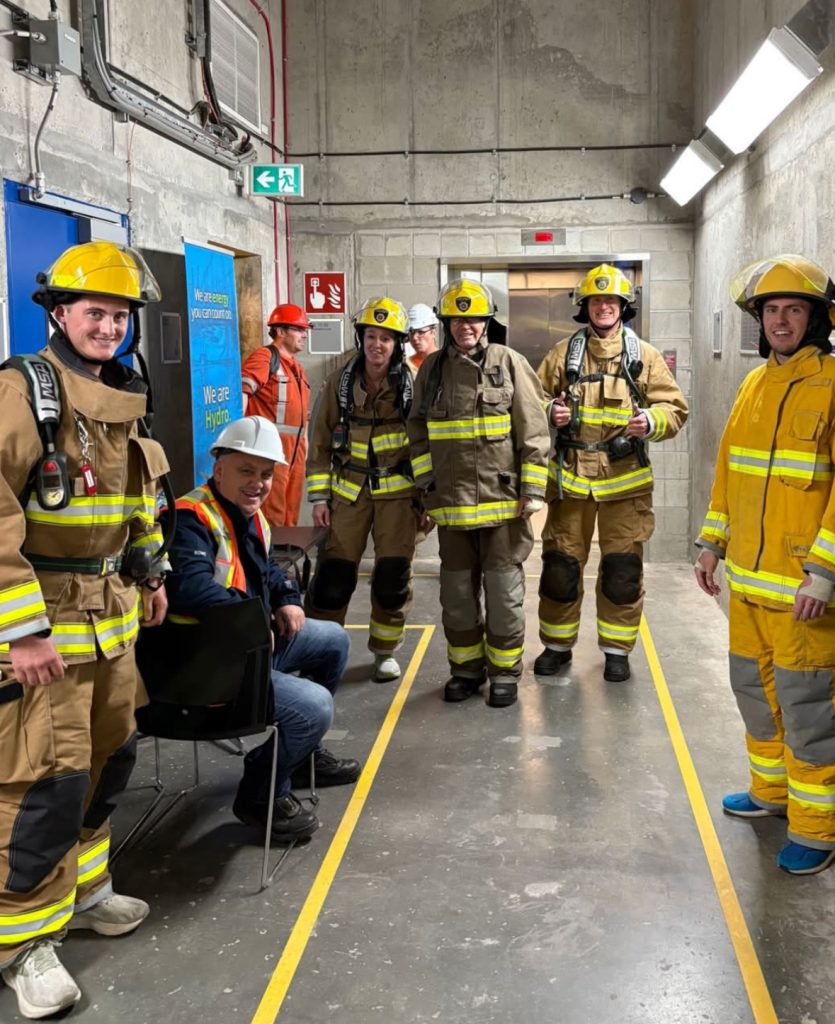 Participants of the Memorial Stair Climb wearing full fire fighting gear stand in a concrete hallway.
