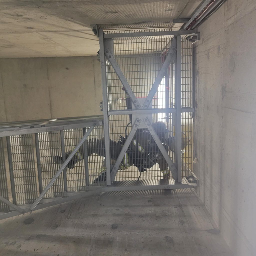 A Stair Climb participant shown from below. They are in a concrete stairwell with metal grate stairs. They are wearing full fire rescue gear.