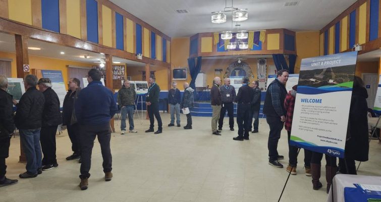 A gathering of people in a large room at the Hydro BDE community open house. The appear to be looking at information boards placed around the room and having conversations.