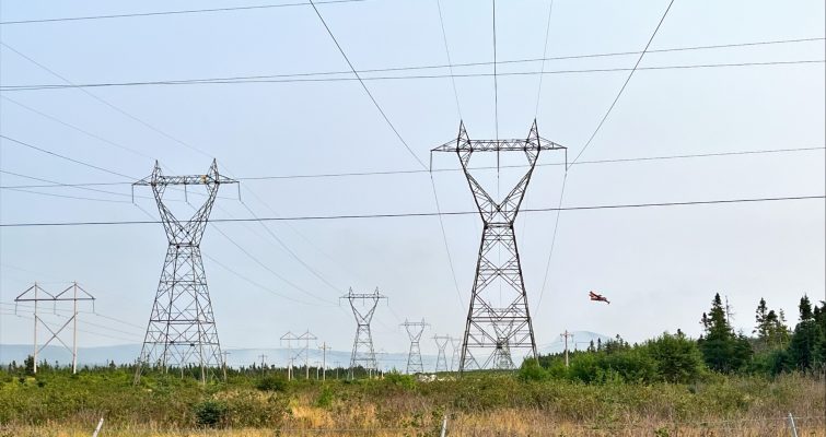 Three transmission lines with a waterbomber flying by in the background.