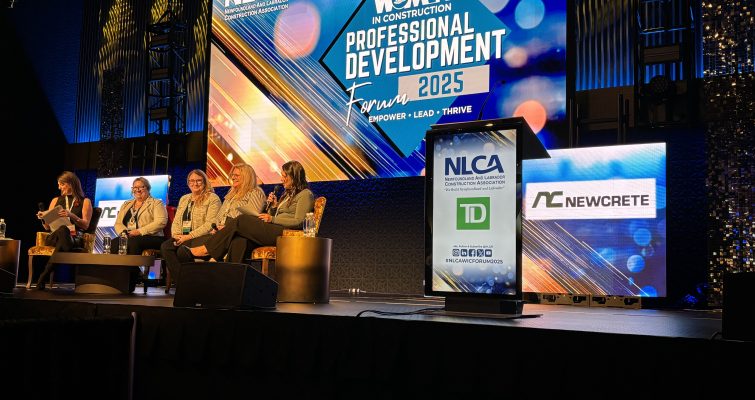 Five panelists sitting on a stage during the conference with 'Women in Construction' on a lit backdrop behind them.