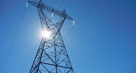 Electricity tower a blue sky and the sun in the background.