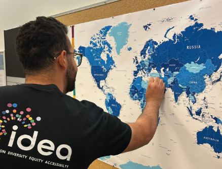 IDEA Ambassador in a black tshirt with the IDEA logo on back, placing a pin on a blue and white map of the world.