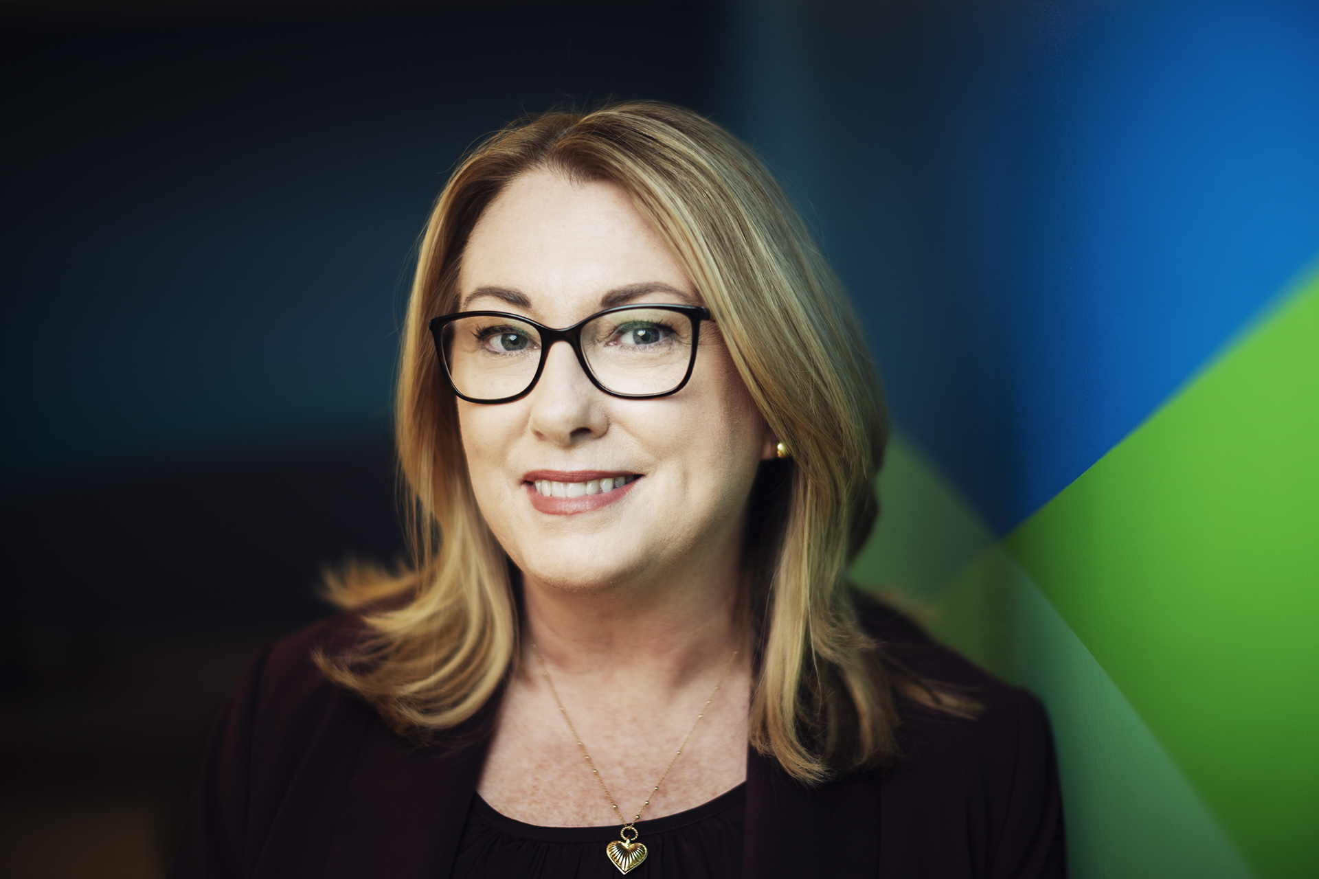 Headshot of CEO Jennifer Williams smiling at the camera in front of a black, green and blue backdrop.